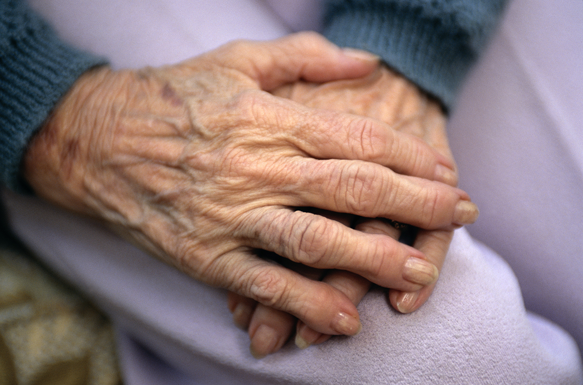 Close-up of an elderly woman's hands resting on her lap.