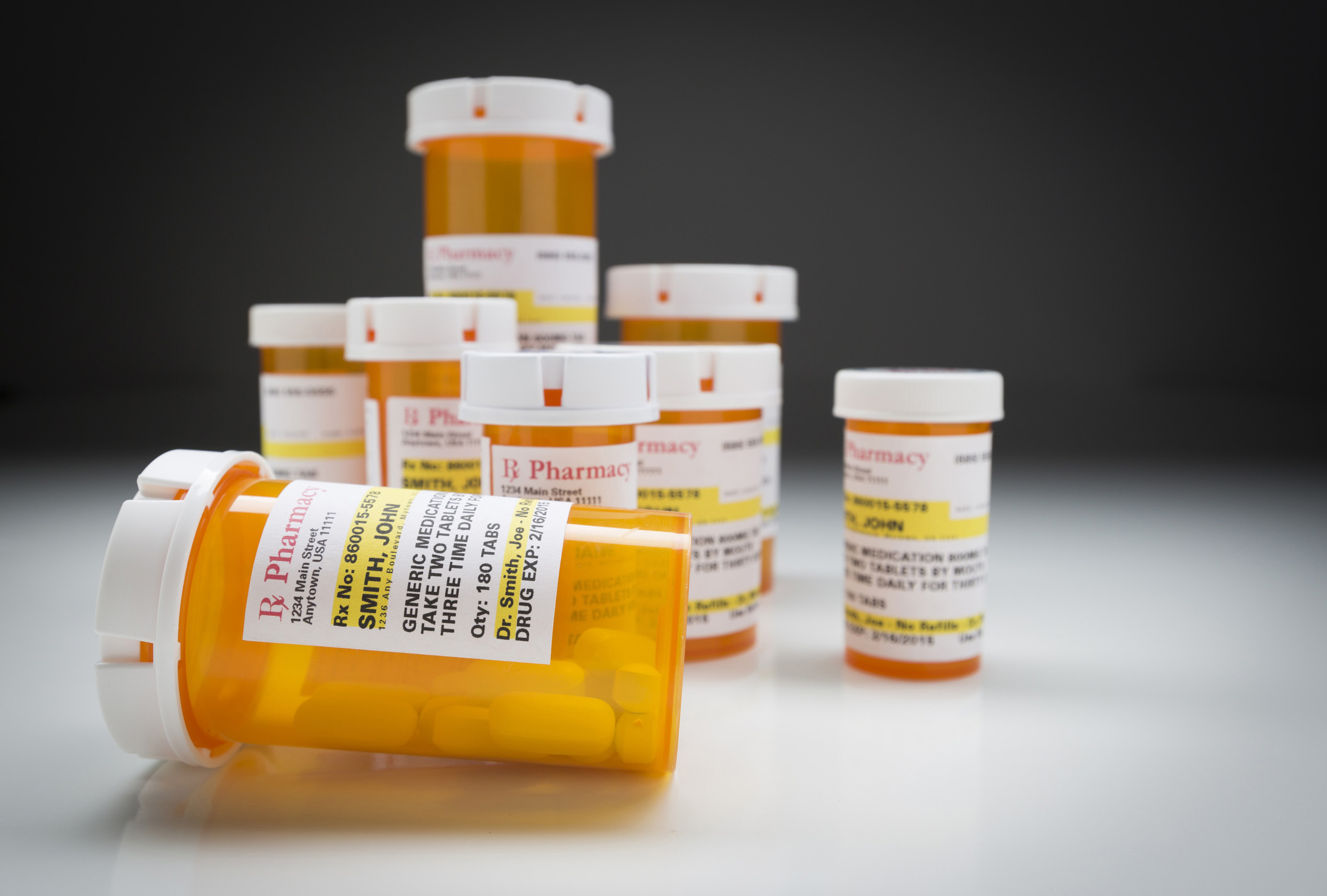 Variety of Non-Proprietary Medicine Bottles on Reflective Surface and Grey Background.