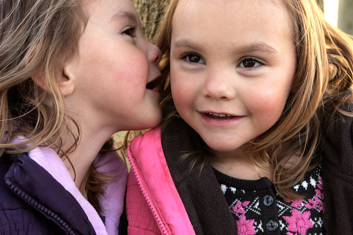 A 3 year old girl whispers a secret into her identical twin sister's ear.