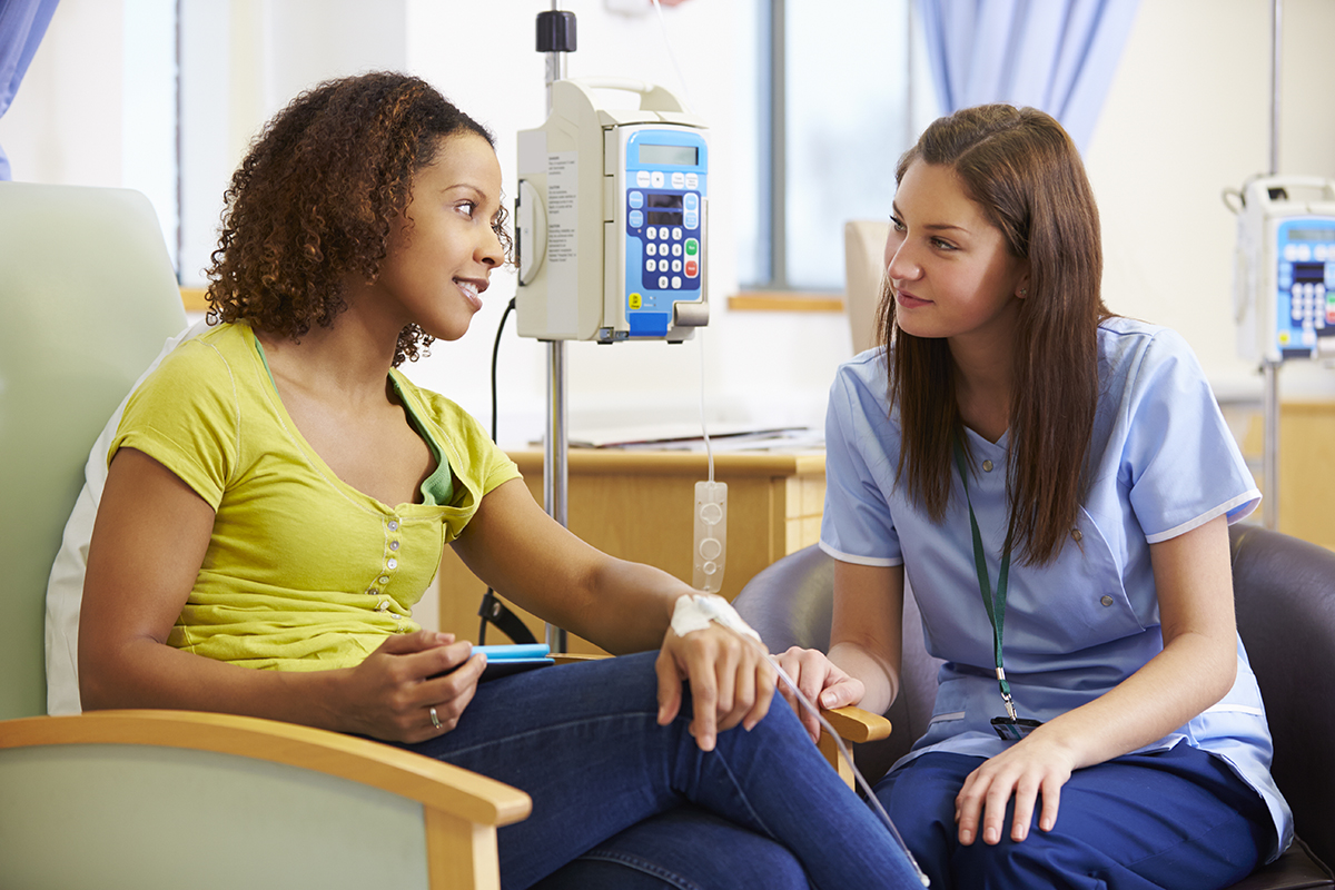 Inclusion in Clinical Trials Female patient and female nurse sit looking at each other while the patient has an IV in her hand.