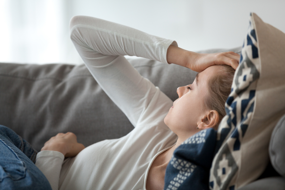 Upset depressed young woman lying on couch feeling strong headache migraine, sad tired drowsy teenager exhausted girl resting trying to sleep after nervous tension and stress, somnolence concept