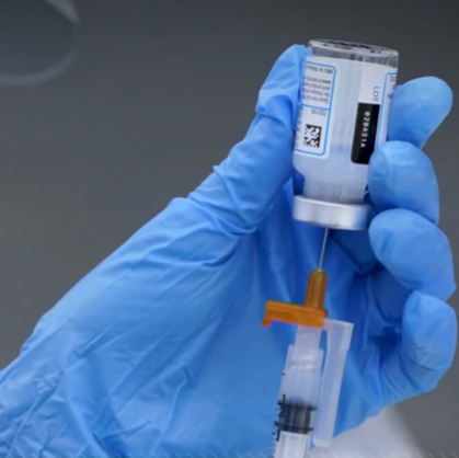 Gloved hand drawing vaccine from vial into syringe