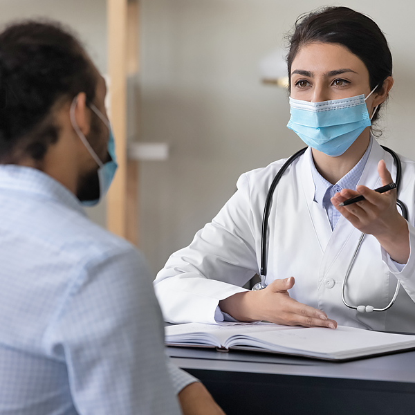 A masked doctor talking to a masked patient
