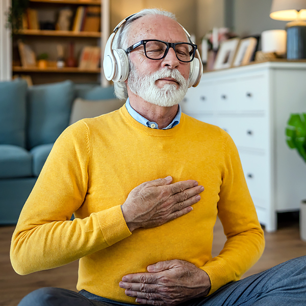 A senior man meditating at home with headphones on