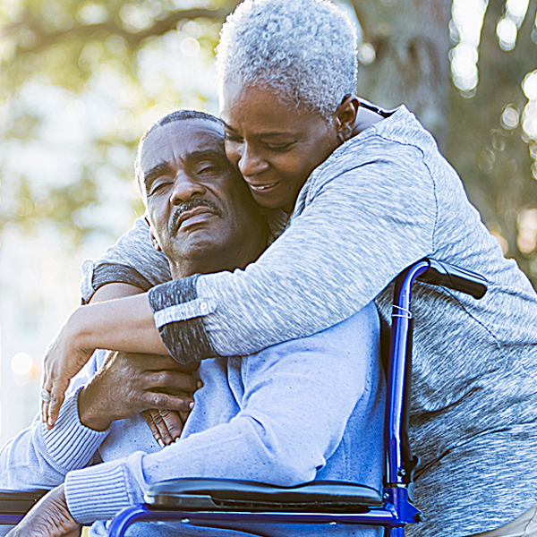 A senior woman embracing a senior man in a wheelchair