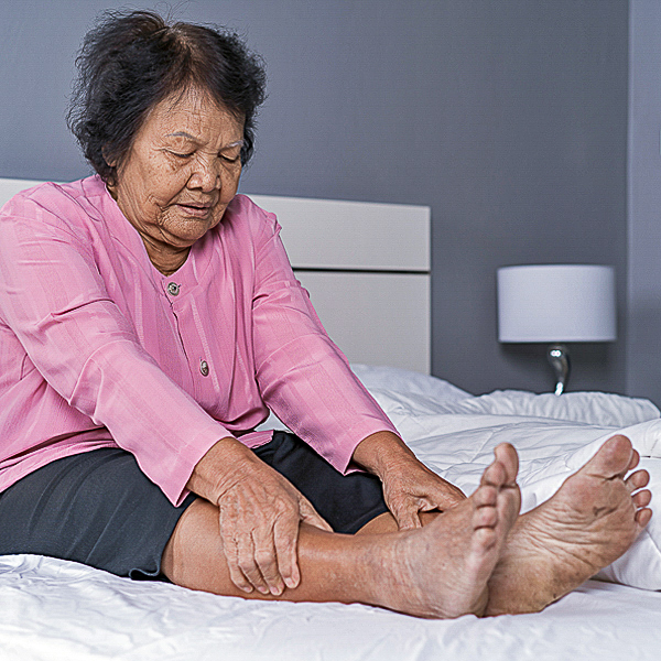 A senior woman sitting in bed and holding her legs