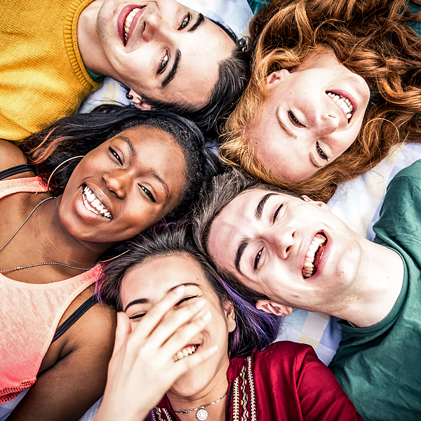 A group of smiling teenagers lying in a circle with their heads touching