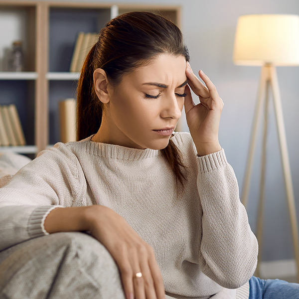 A woman with her eyes closed sitting on a couch and holding her head