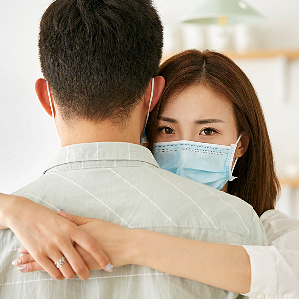 A young woman with a face mask on hugging a man
