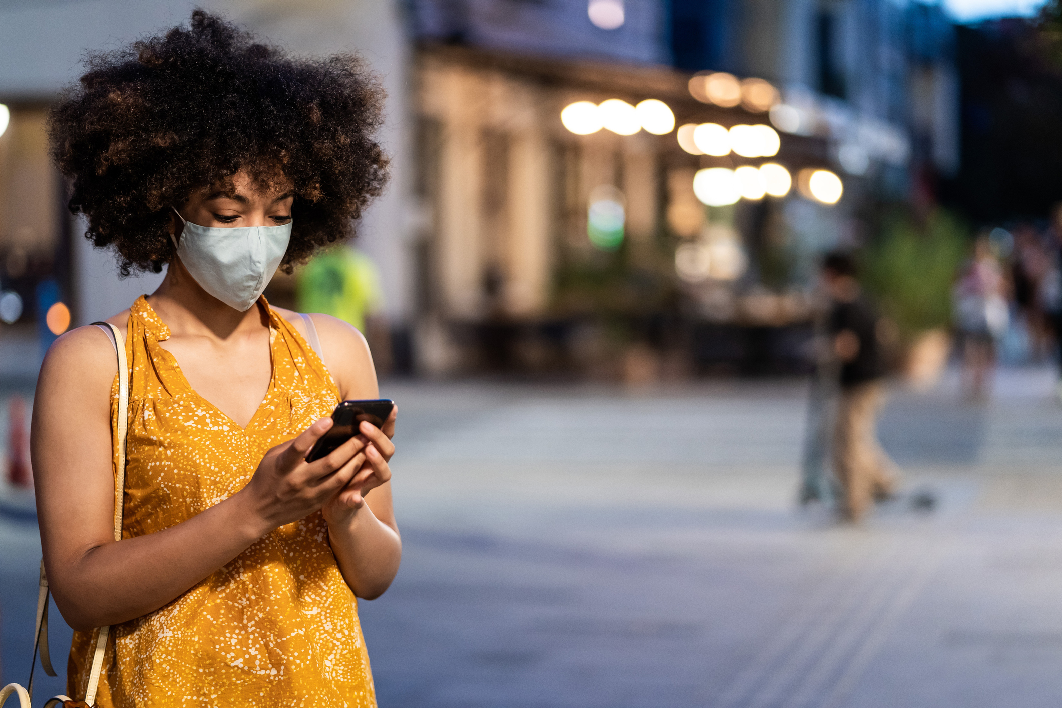 Black women with protective face mask using a smart phone on the street Black women with protective face mask using a smart phone on the street