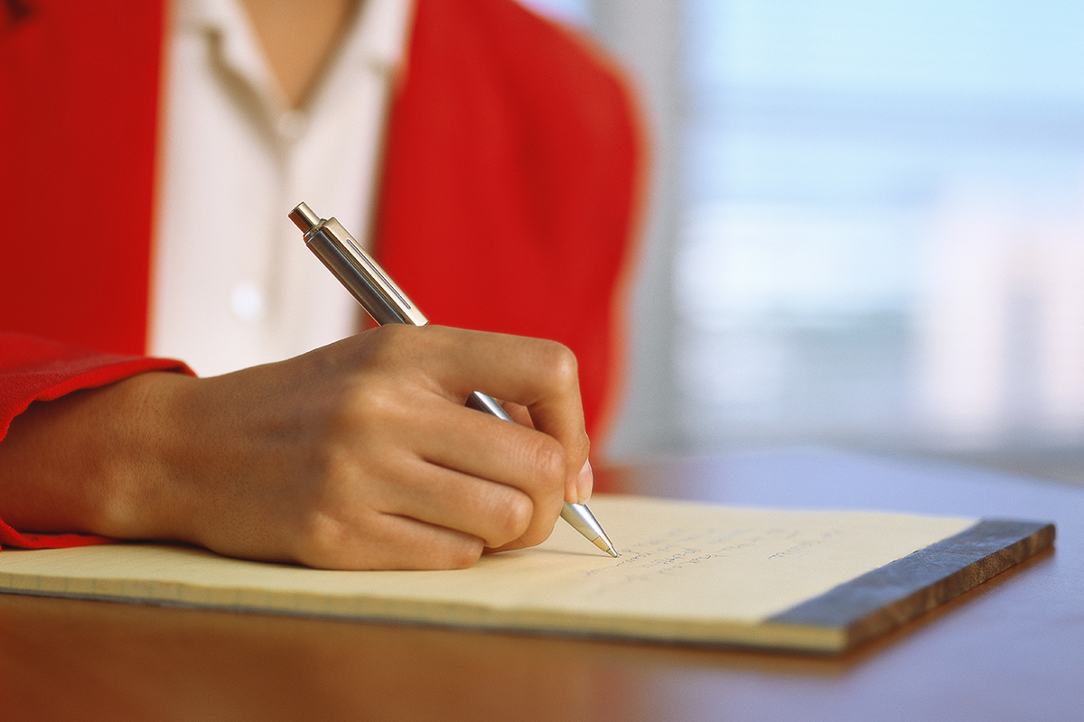 Close-up of a woman writing on a pad.