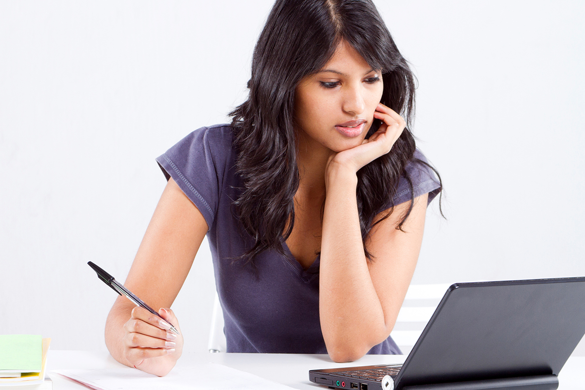 Close-up of a woman with a laptop and a writing pad.