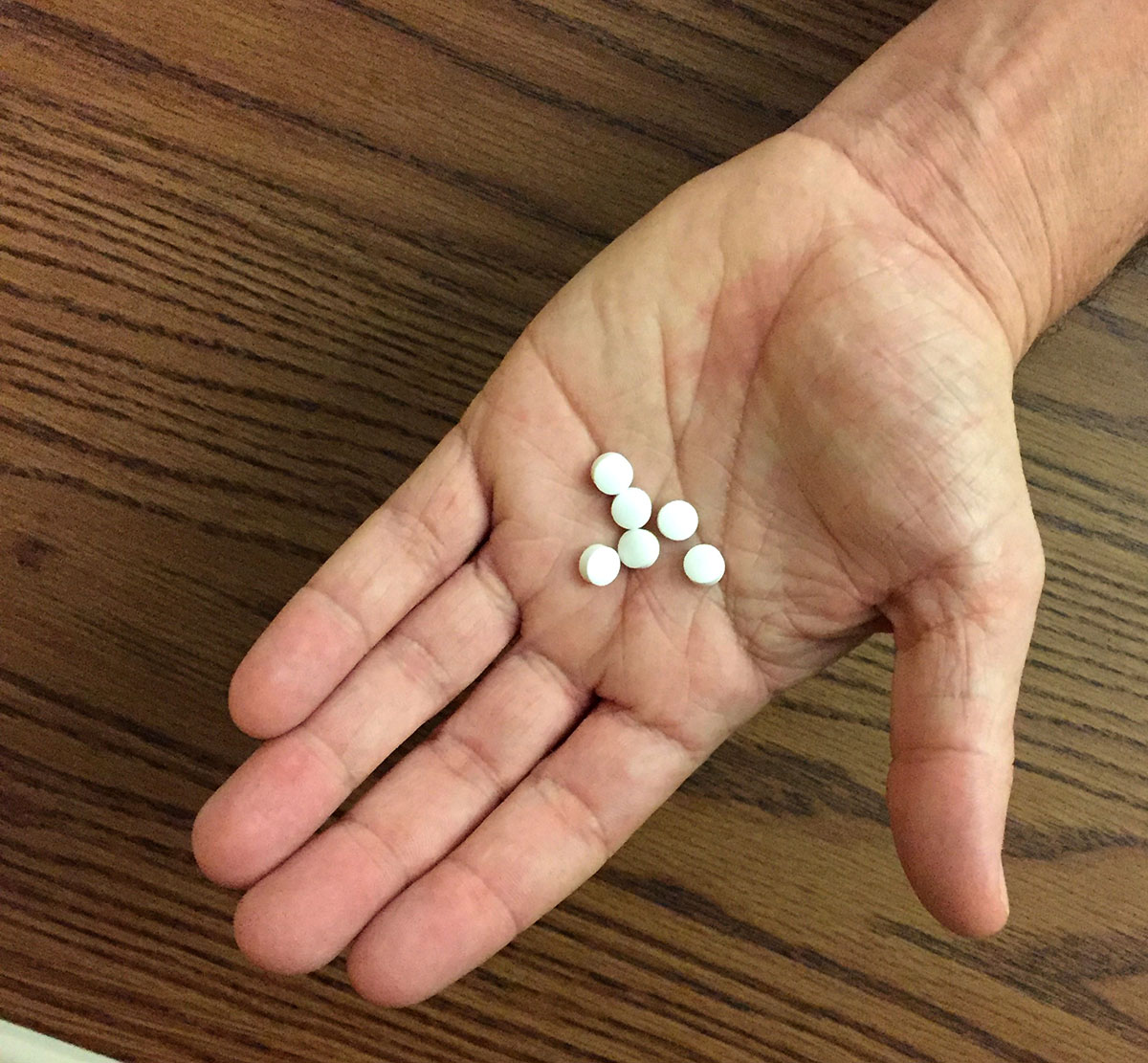 Hand holding six white pills