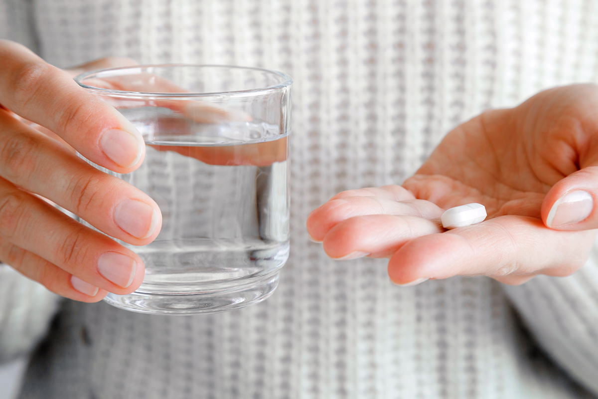 Close up of a person holding a pill and glass of water
