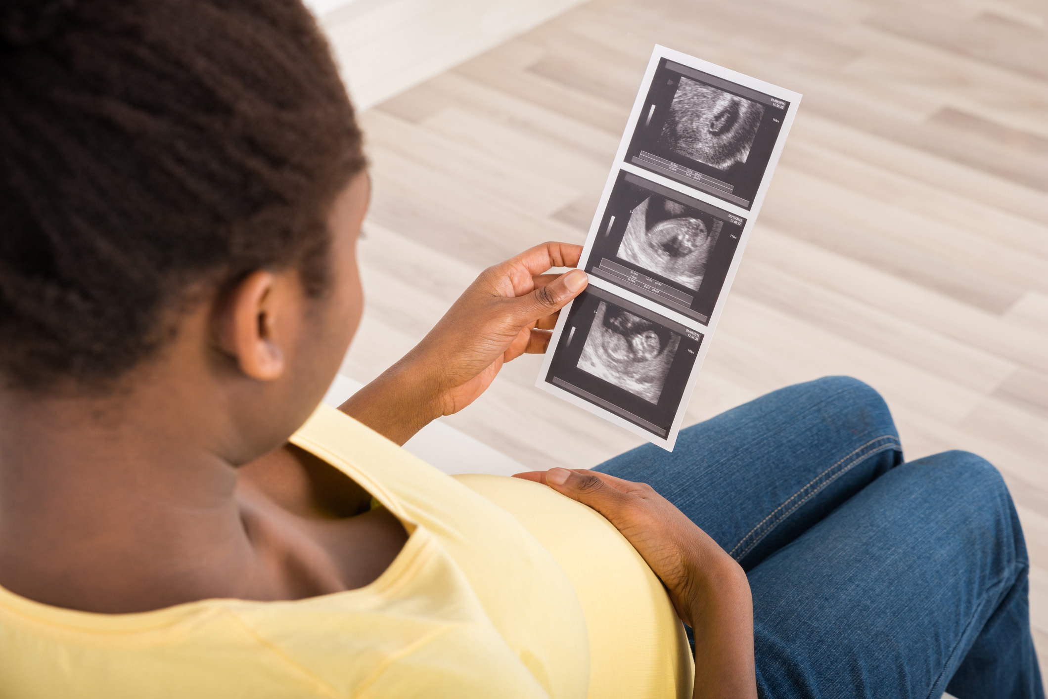 Close-up Of Pregnant Woman Sitting On Sofa Looking At Ultrasound Scan