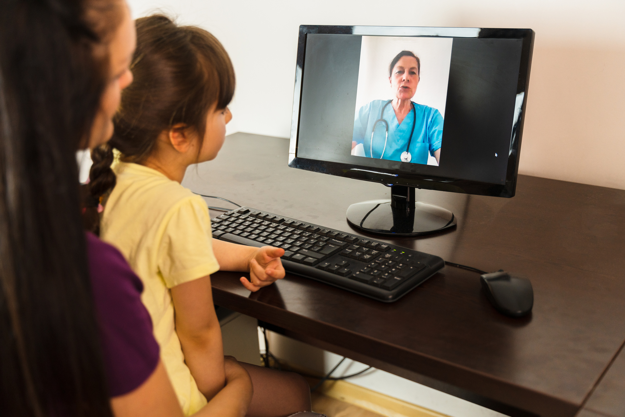 Mother with her daughter video calling doctor from home - stock photo