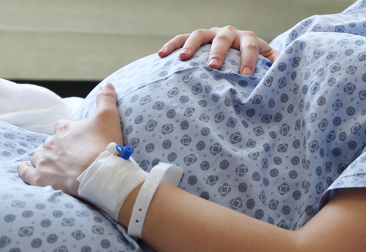 Closeup of pregnant mother in a hospital gown holding her belly