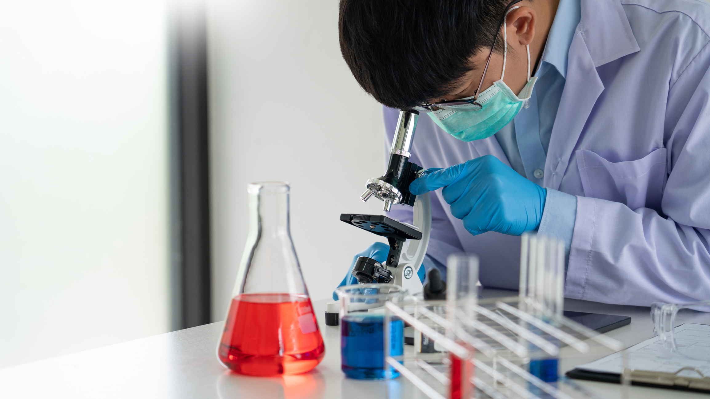 Attractive young scientist team in lab coat and safety goggles working with analysing test trial or investigations with test tubes in laboratory - stock photo