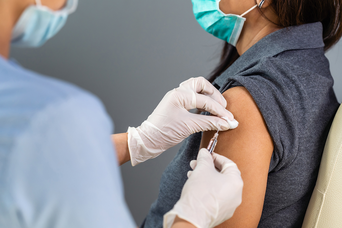 Close up of a medical professional administering a vaccine to a patient in a medical mask