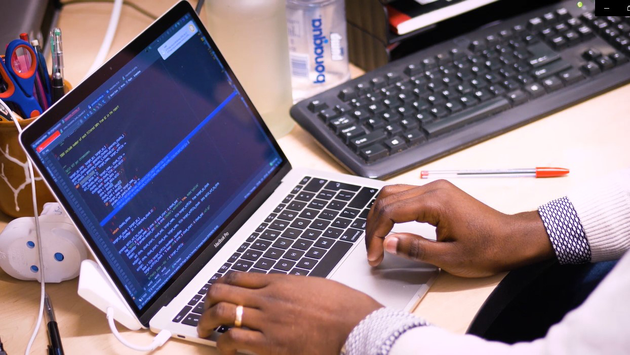 hands typing on a laptop with data on screen and another keyboard nearby