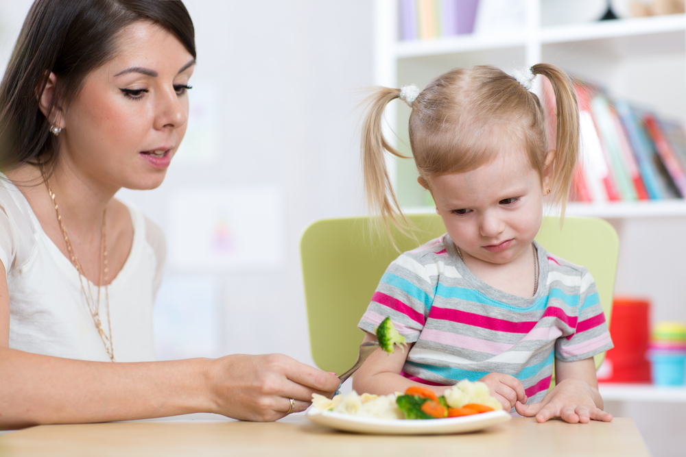 Child girl looks with disgust at healthy vegetables. Mother convinces her daughter to eat food.