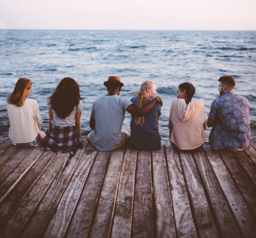 Young multi-ethnic hipster friends and couples sitting on wooden jetty - stock photo
