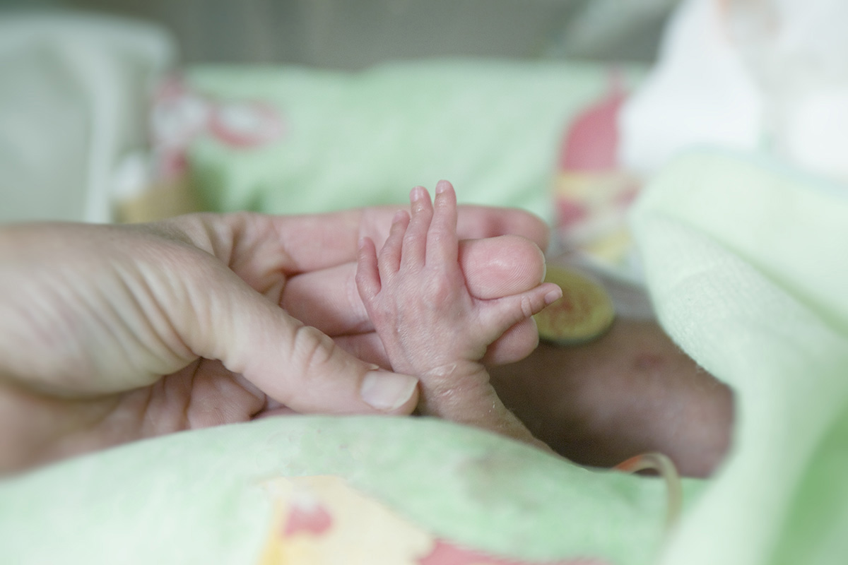 tiny infant hand grasping adult fingers