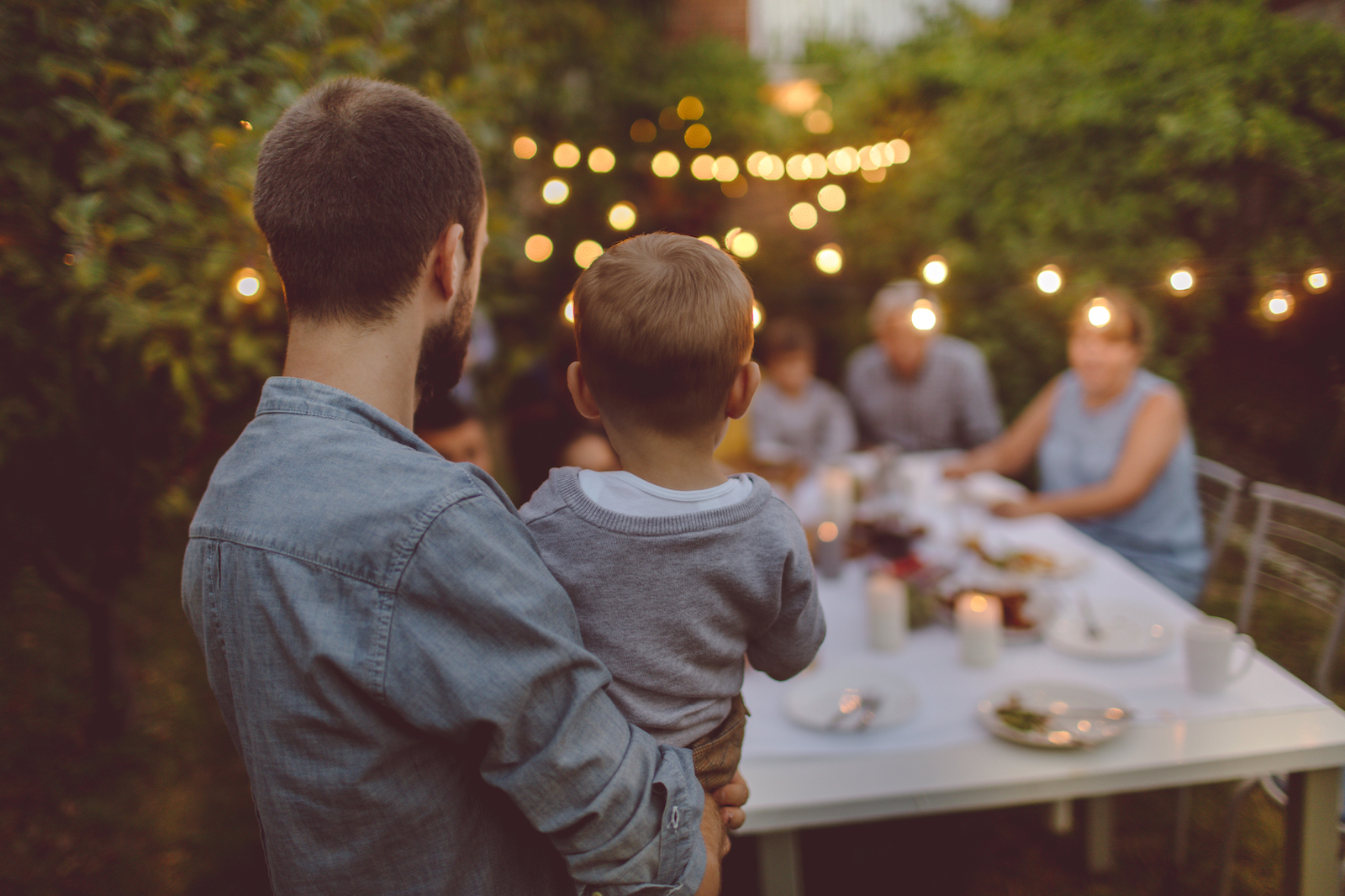 A man holding a child looking at a table with family around it.