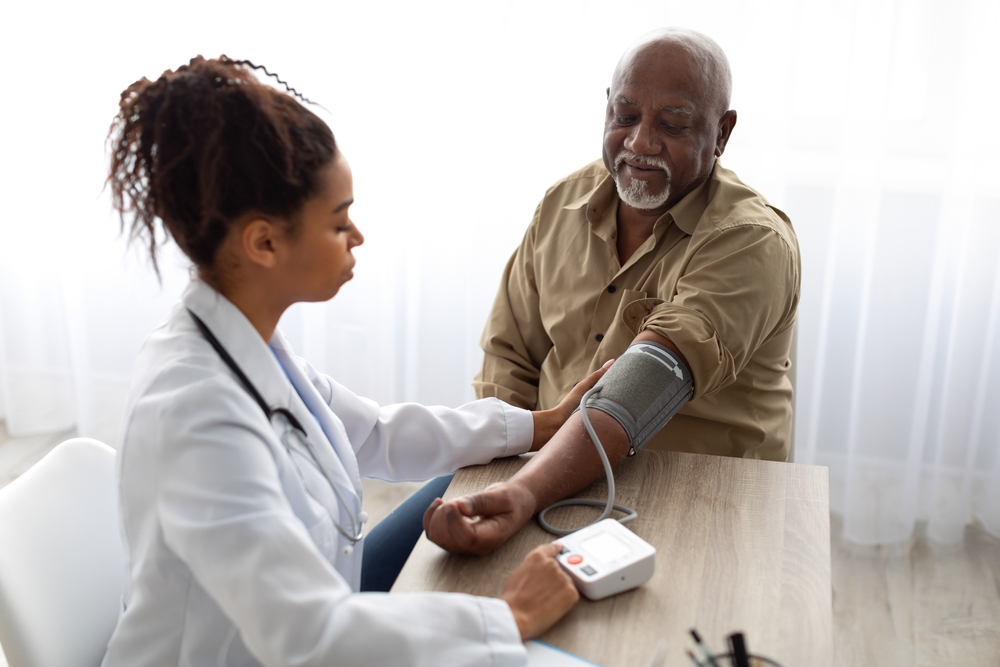Hypertension In Older Age. Young Female Medical Worker Measuring Arterial Blood Pressure Of Senior Black Man Using Cuff, Patient Having Problems With Tension Hypertension In Older Age. Young Female Medical Worker Measuring Arterial Blood Pressure Of Senior Black Man Using Cuff, Patient Having Problems With Tension