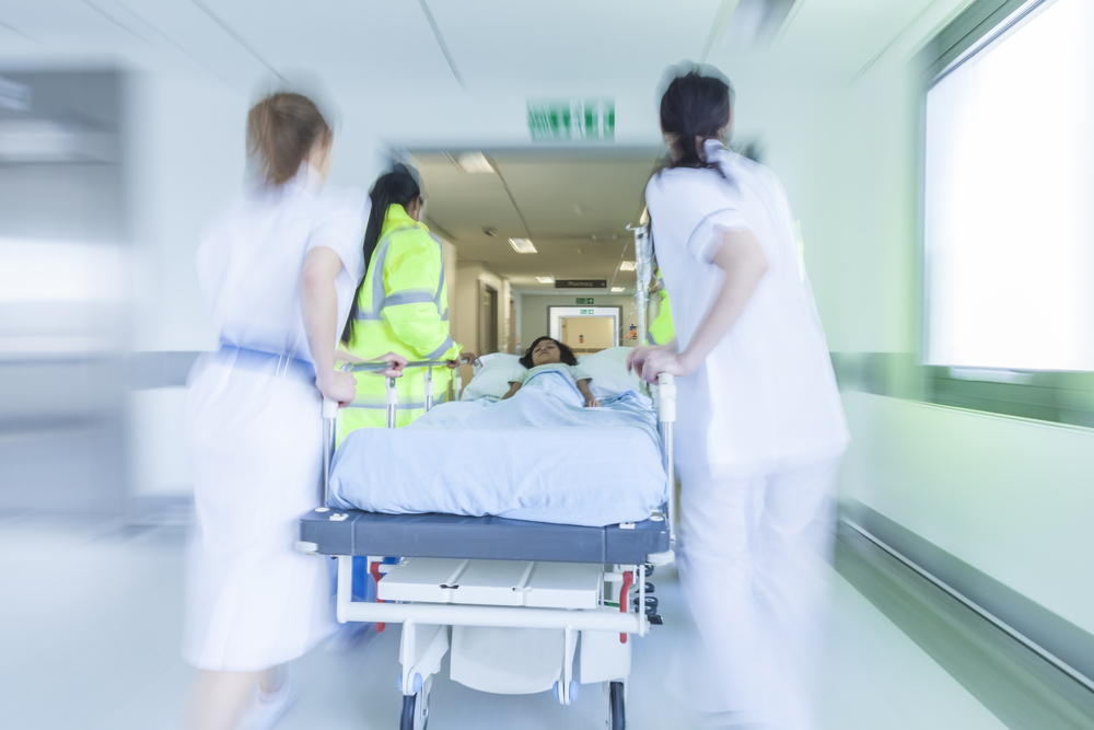 A motion blurred photograph of a child patient on stretcher or gurney being pushed at speed through a hospital corridor by doctors & nurses to an emergency room