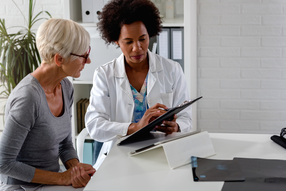 A female doctor sits at her desk and chats to an elderly female patient while looking at her test results