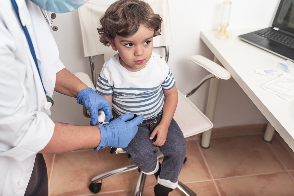 Paediatrician takes blood sample from toddler to check glucose levels.