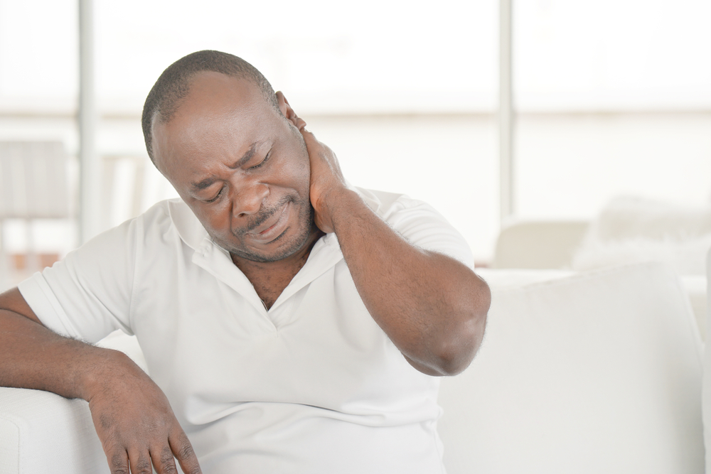 Elderly african man suffering from neck pain at home on couch. Males sense of fatigue, exhausted, stressed. African man massages her painful neck with her hands. The concept of body and health.