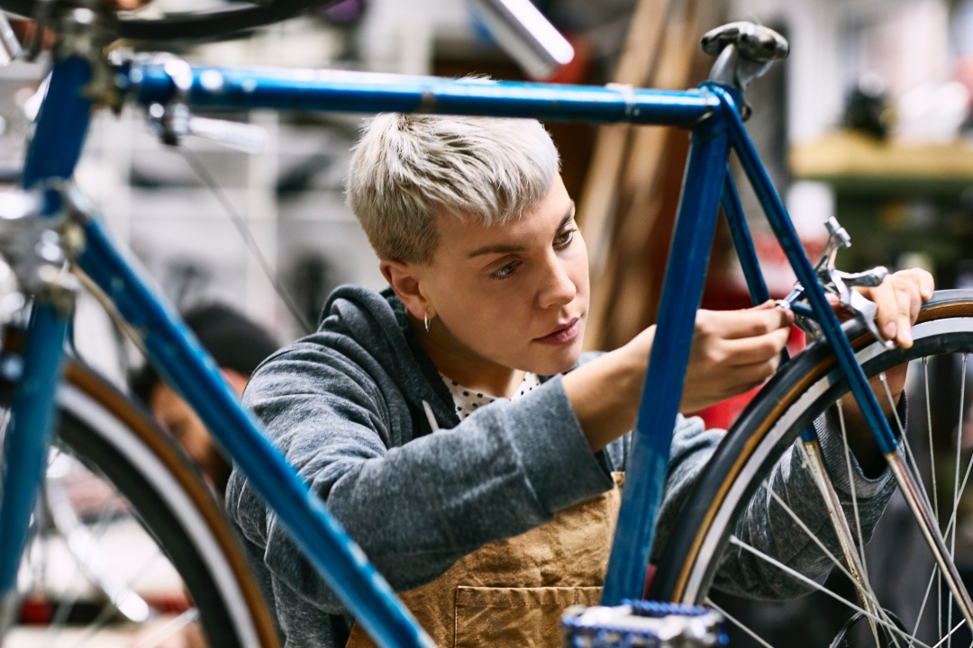 A young adult employee in a bike shop tightens the brakes on the back wheel of a road bicycle. A young adult employee in a bike shop tightens the brakes on the back wheel of a road bicycle.