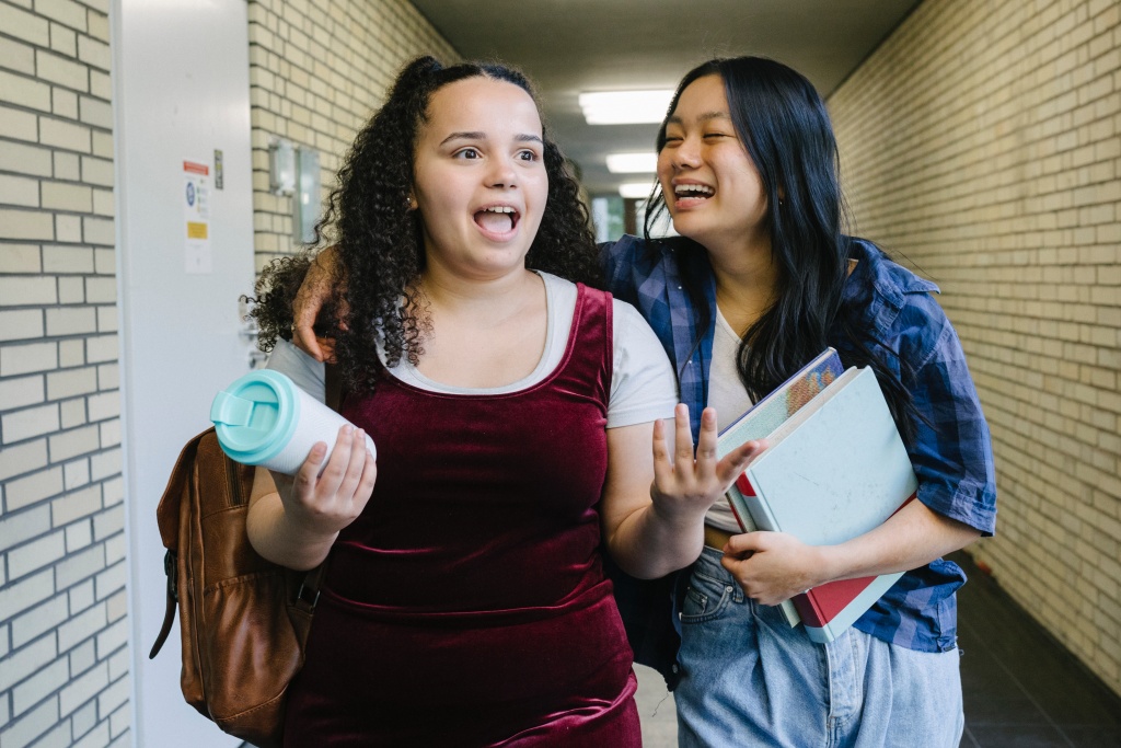 Image of two teenage girls talking and walking together down a classroom hallway during a school day.