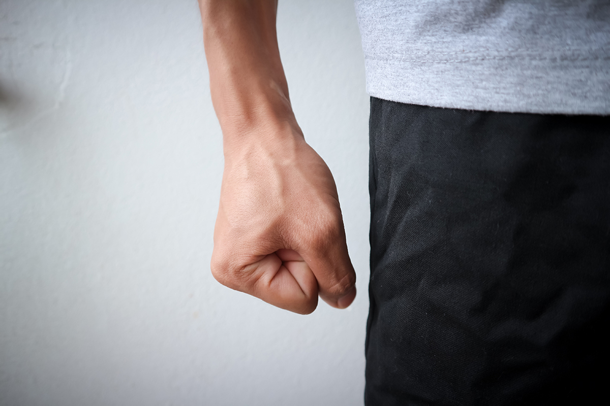 Fist of angry man wearing a gray shirt and black pants who is experiencing blood vessel strain Fist of angry man wearing a gray shirt and black pants who is experiencing blood vessel strain