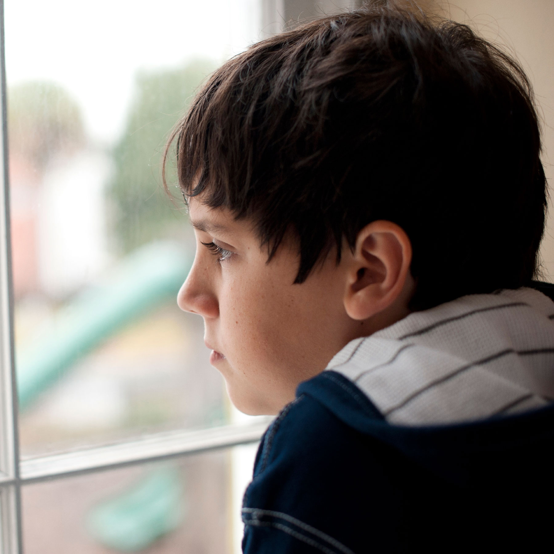 Photo of a young boy looking out a window cropped