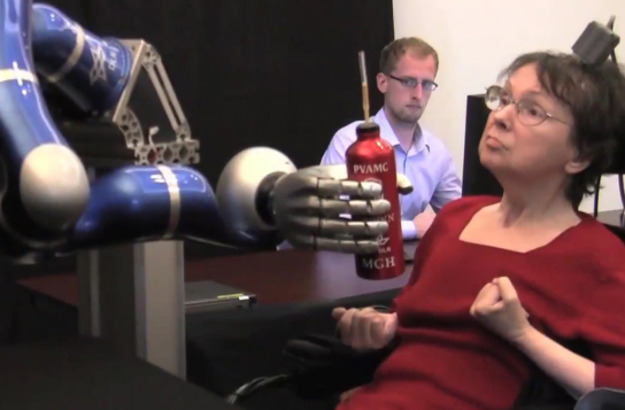 A woman controlling a robotic arm to grasp a bottle.