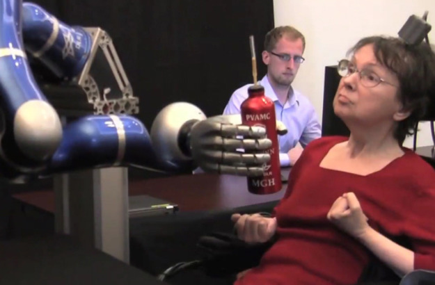 A woman controlling a robotic arm to grasp a bottle. A woman controlling a robotic arm to grasp a bottle.