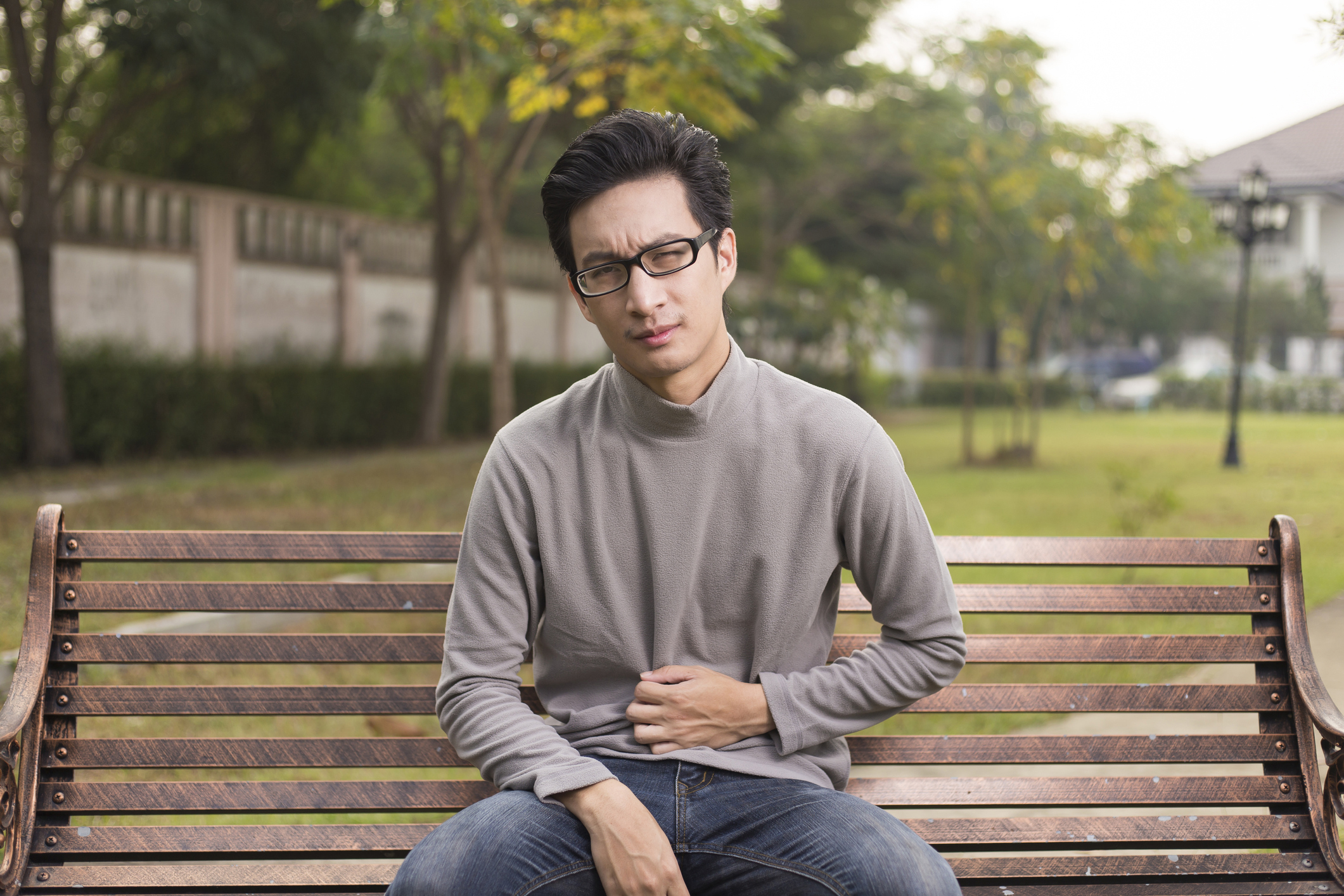Man on park bench holding his stomach in discomfort Man on park bench holding his stomach in discomfort