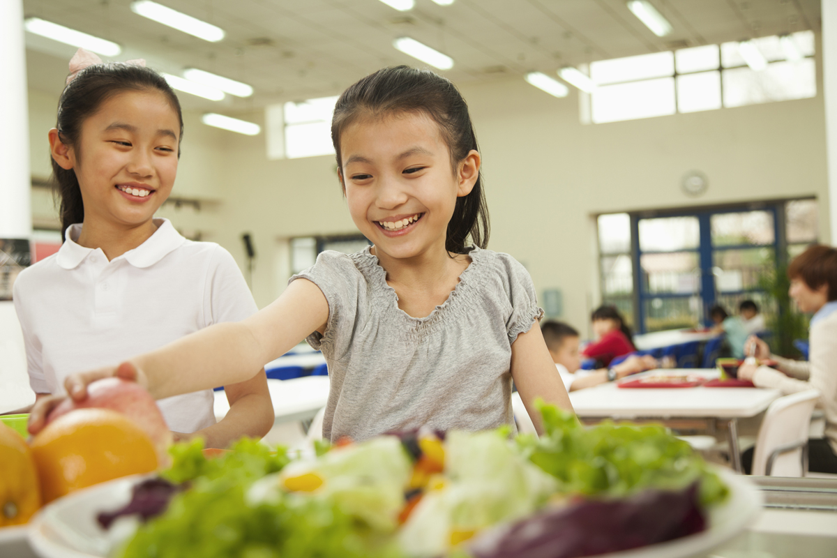 Students reaching for healthy food in school cafeteria.