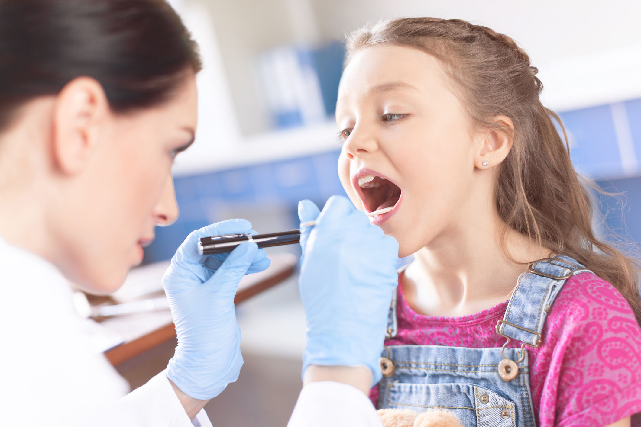 Woman doctor examining girl’s throat with spatula and flashlight