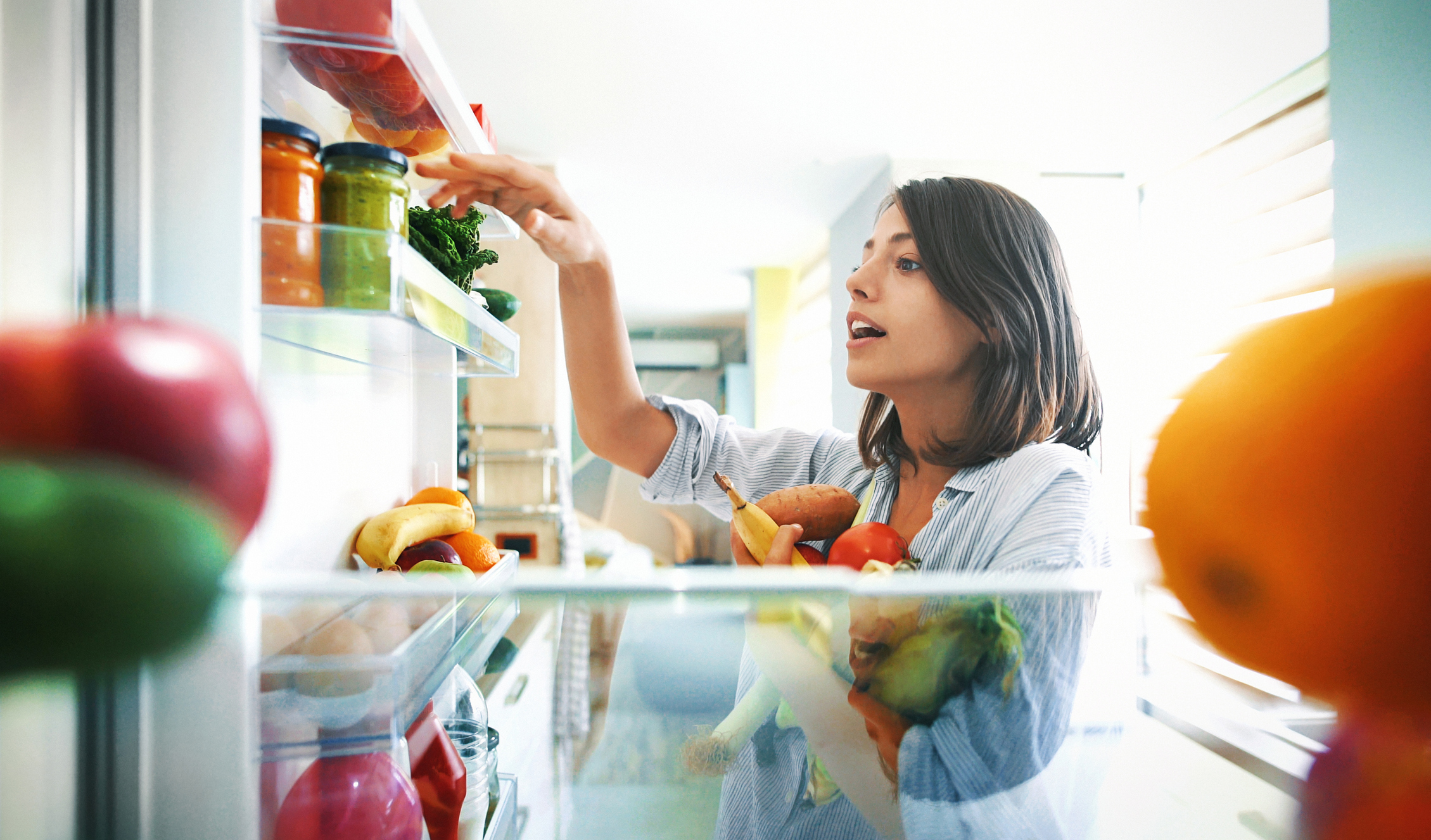 Woman picking fruits and veggies from the fridge