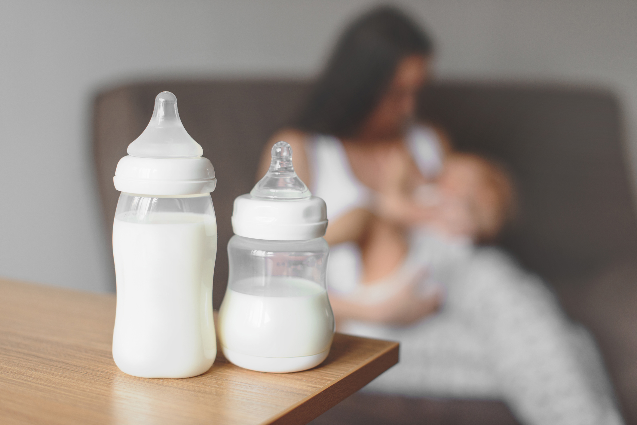 Bottles of breast milk with mother breastfeeding baby in the background
