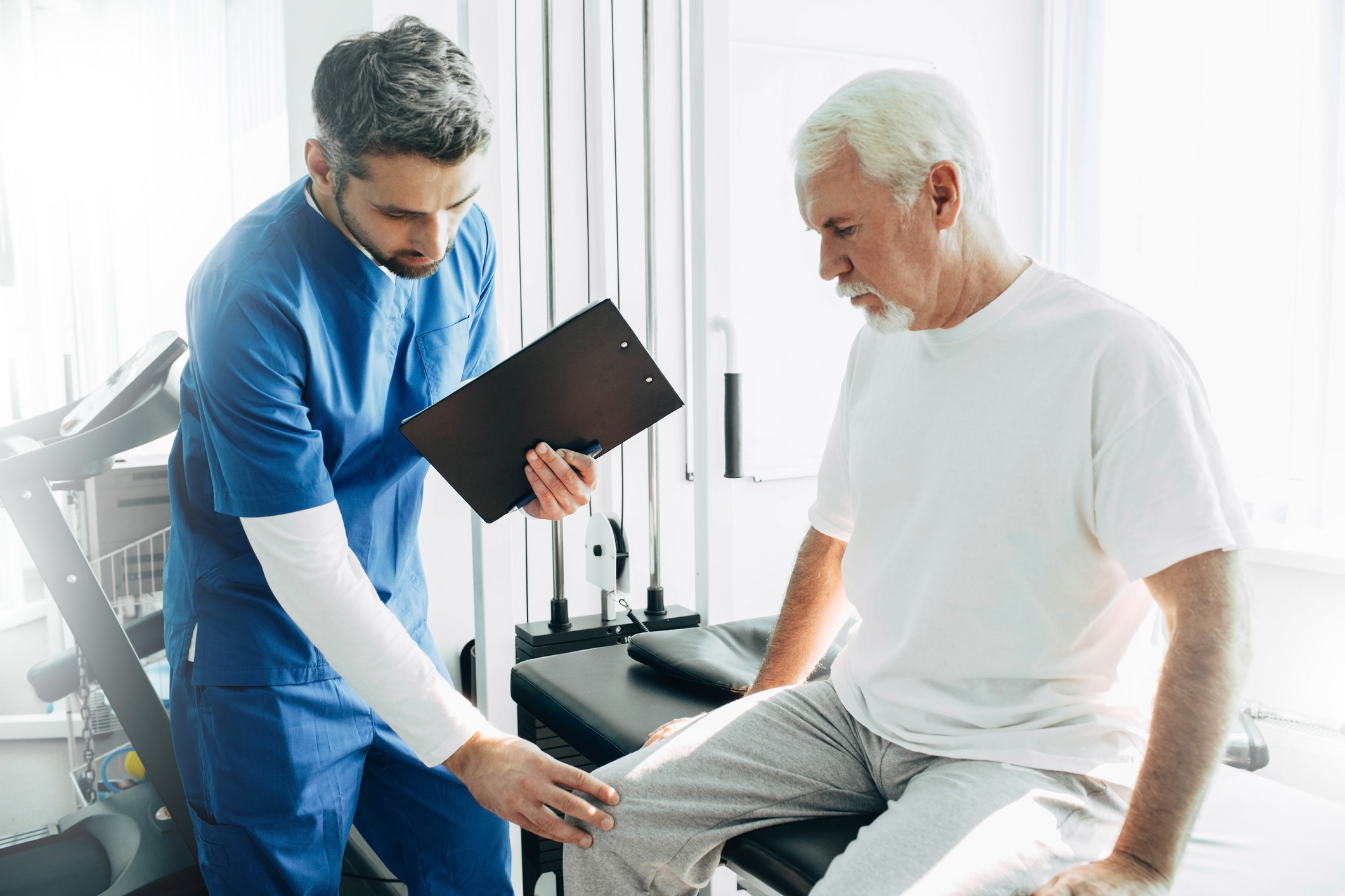 Health professional examining senior man’s knee.