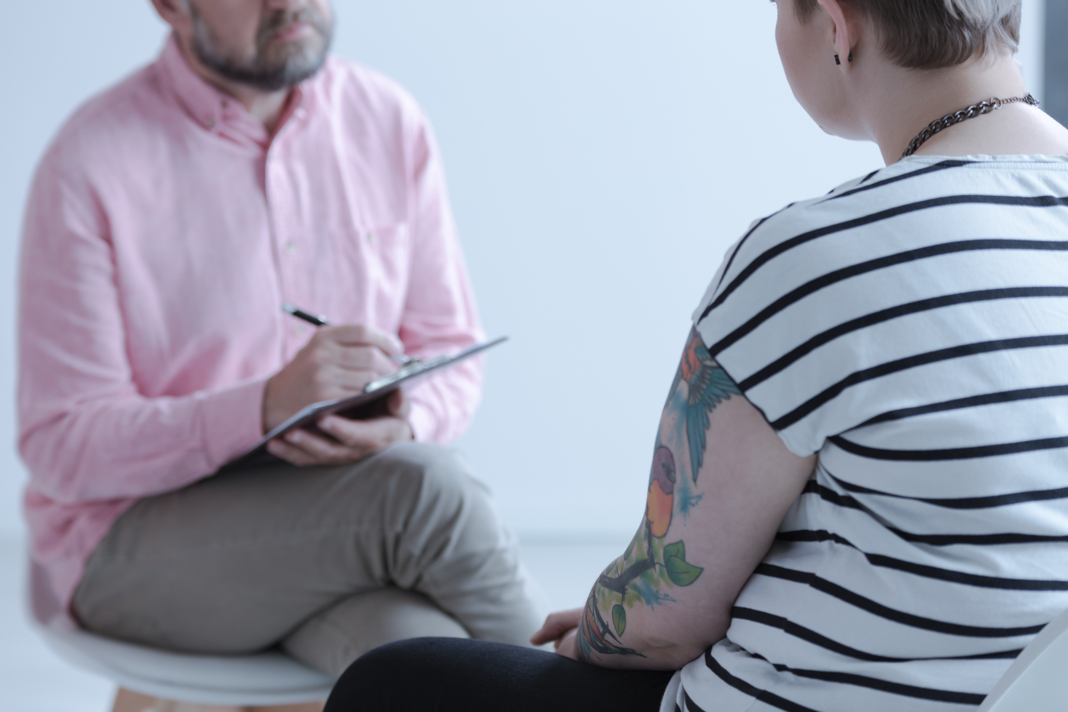 Therapist taking notes while listening to a tattooed young person