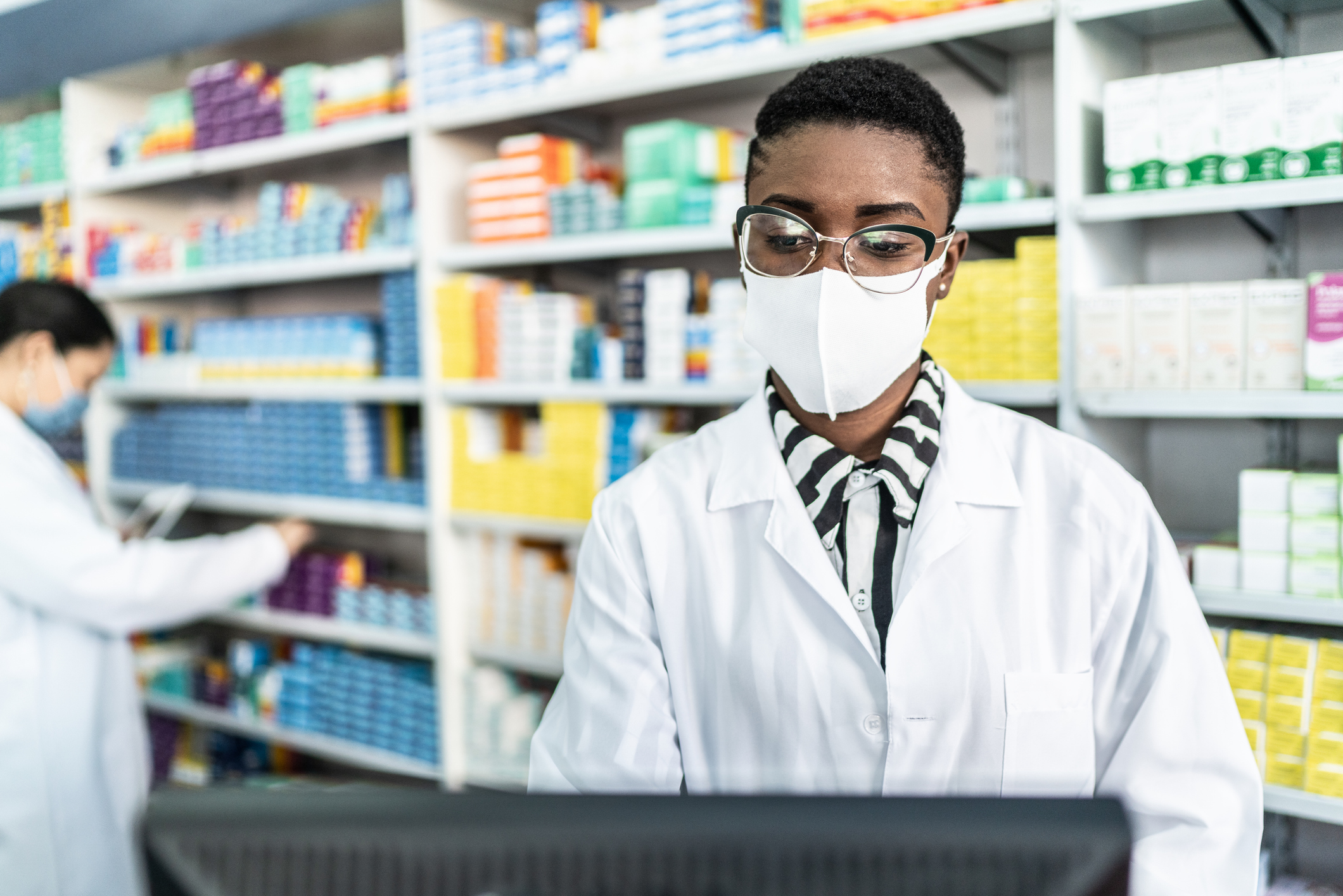Female pharmacist with face mask at a computer
