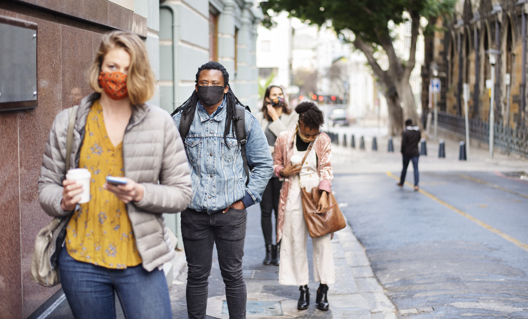 Diverse group of people wearing protective face masks practicing social distancing while waiting in a line on a city sidewalk