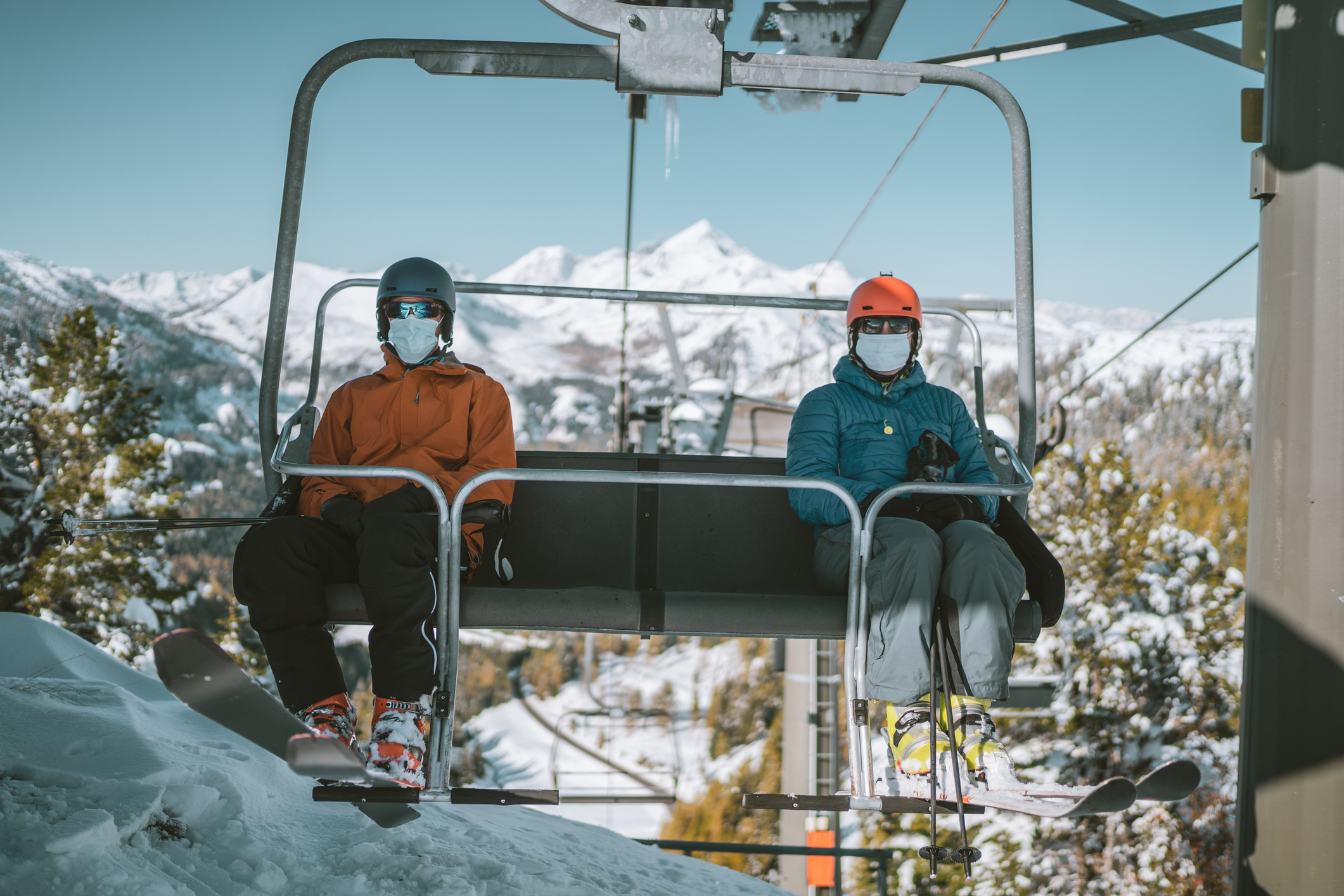 Two skiers with face masks on each side of a chair lift