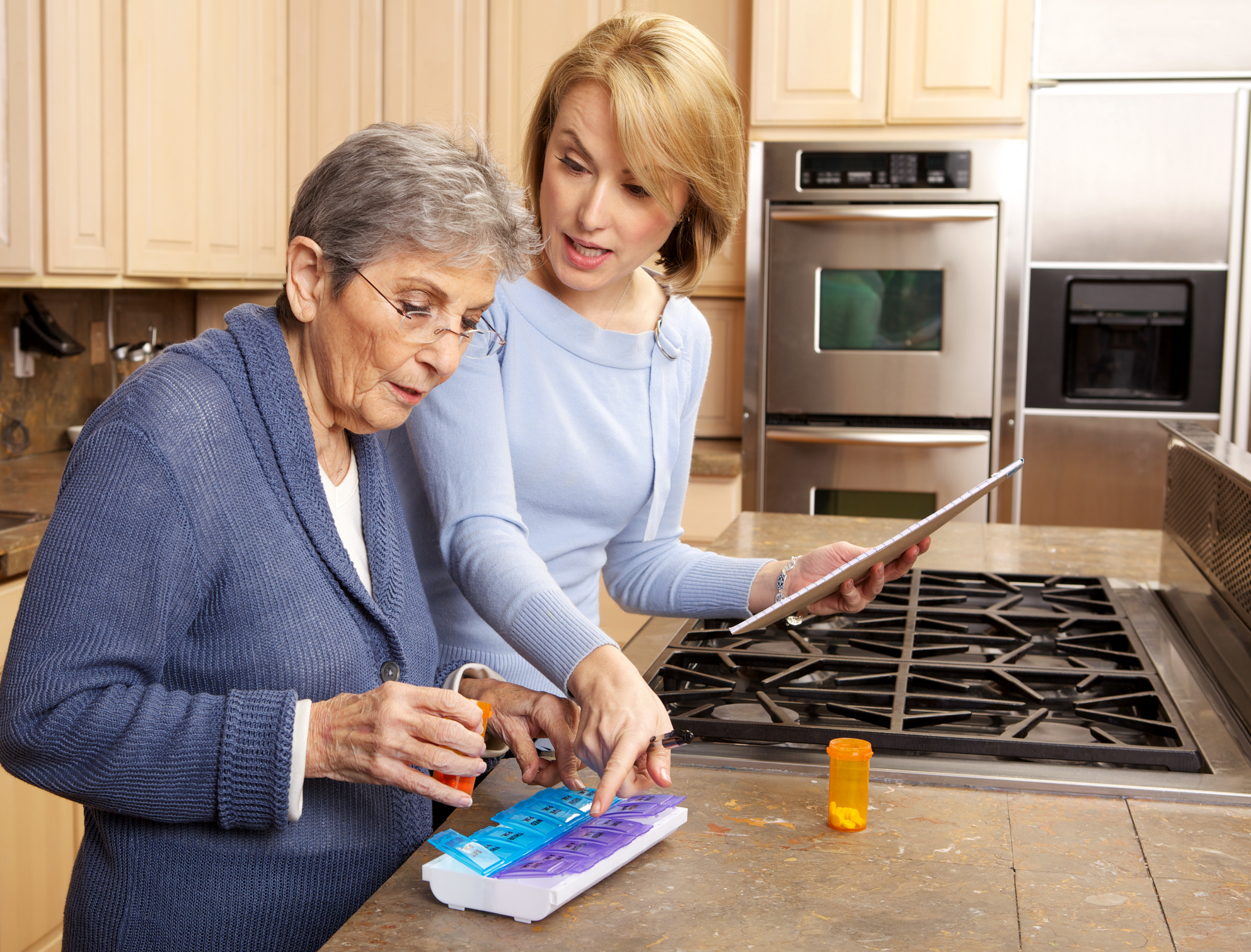 Young woman helping senior in kitchen to sort her medications